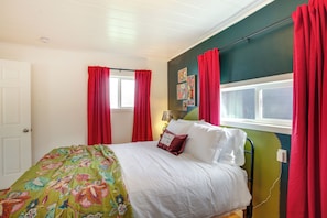 Een slaapkamer met een bed, rode gordijnen, een groene muur en een raam.