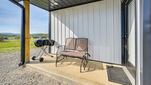 Eine Terrasse im Freien mit einer Metallbank und einem Grill, ein Betontrittstufen zum Eingang und Blick auf die Landschaft.