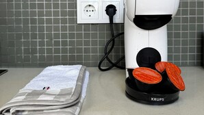 Una macchina da caffè bianca con base nera, una presa di corrente e un asciugamano piegato su un piano di lavoro.