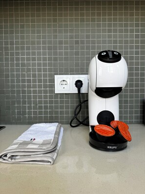 Eine weiße Kaffeemaschine mit schwarzem Fuß, eine Steckdose und ein gefaltetes Handtuch auf einer Arbeitsplatte.