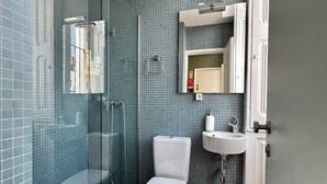 Un bagno moderno con cabina doccia in vetro, un water, un lavandino e pavimento in legno.