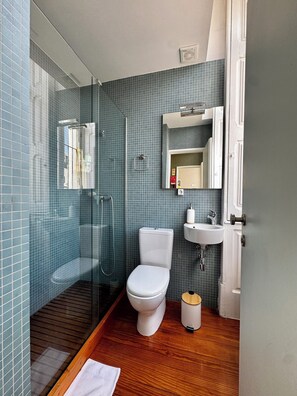 Ein modernes Badezimmer mit Duschkabine aus Glas, Toilette, Waschbecken und Holzboden.