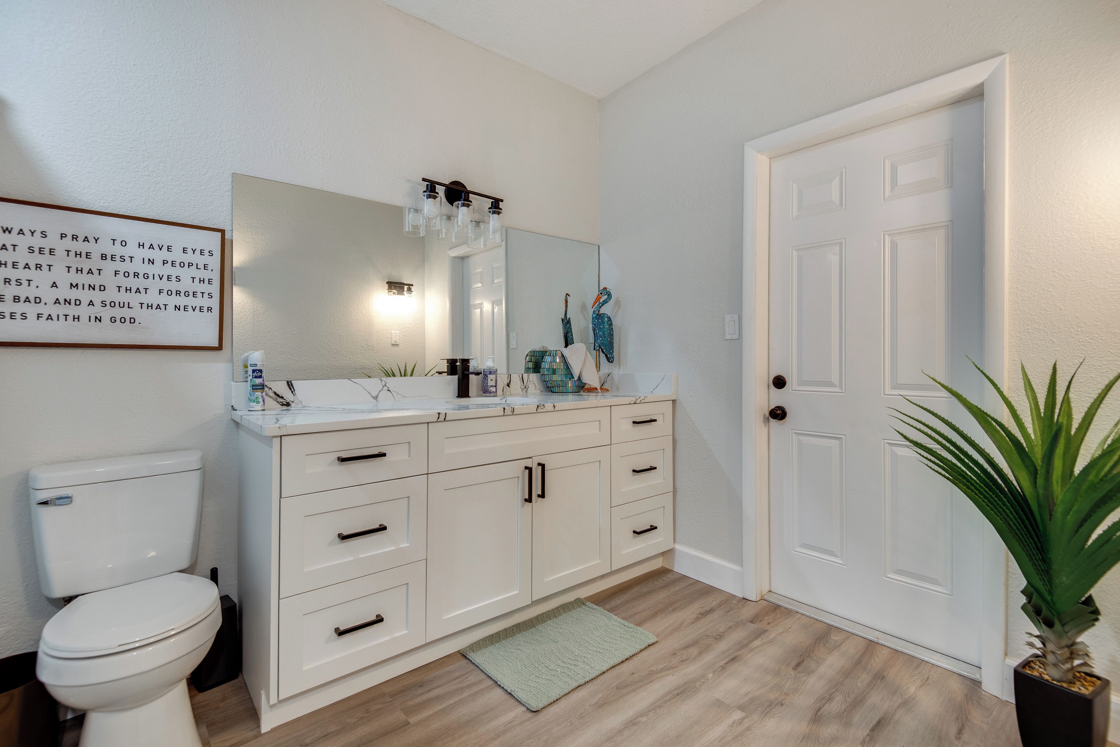 A bathroom with a toilet, a sink with a mirror, a cabinet, and a door.