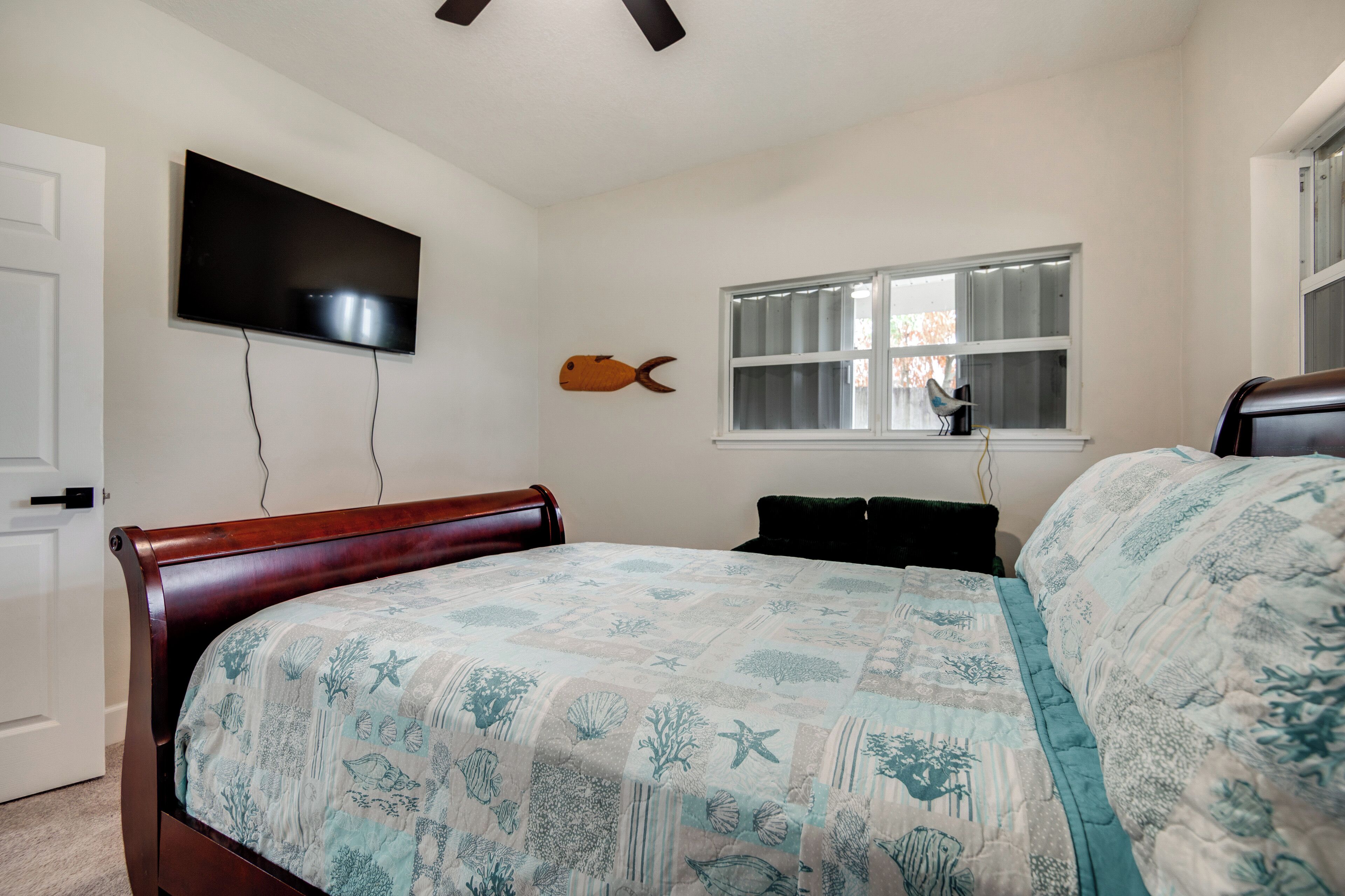 Un dormitorio con cama, televisor montado en la pared, ventana con persianas y un pez decorativo en la pared.
