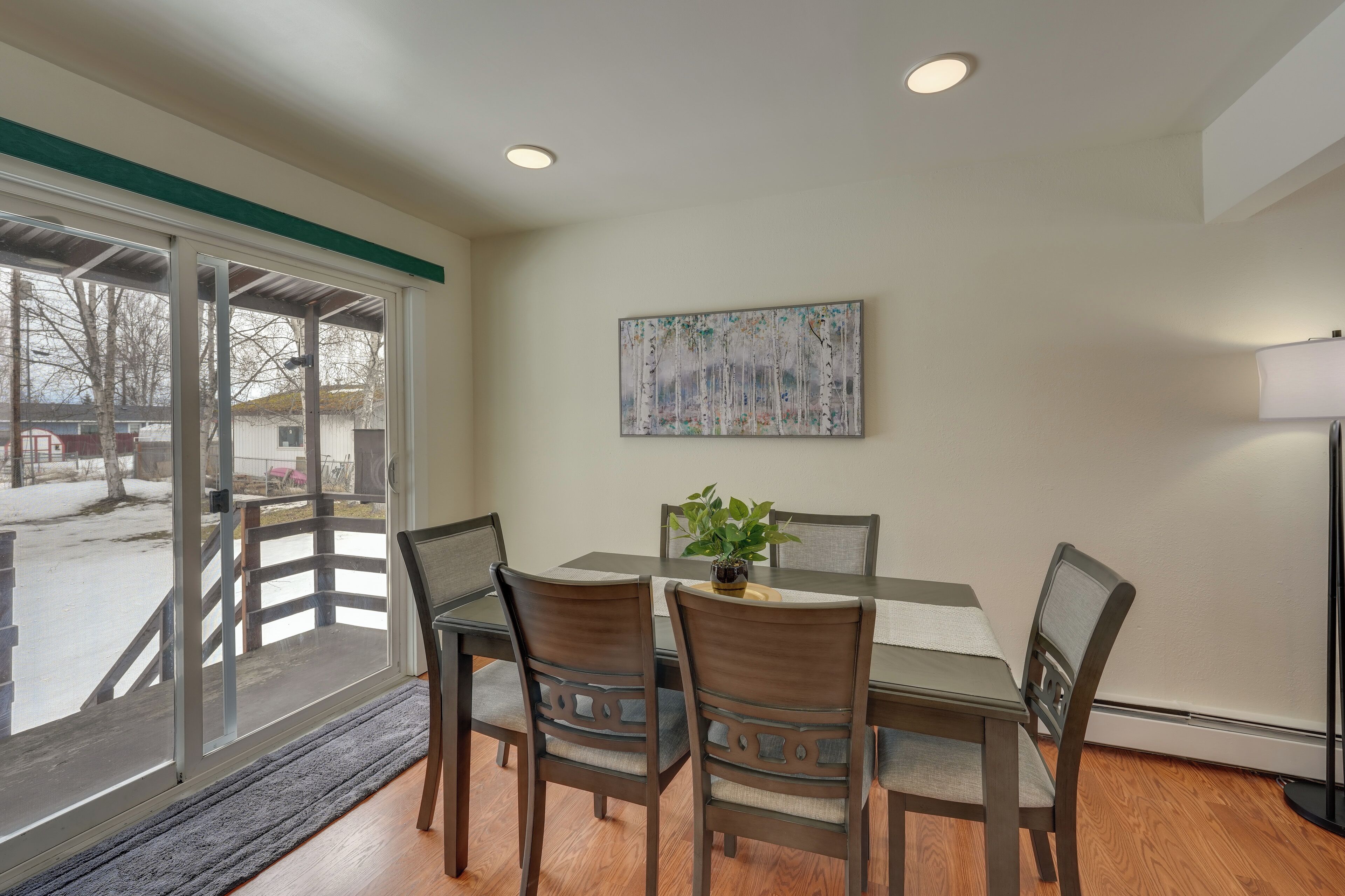 A dining area with a table, chairs, a plant, and a painting on the wall.