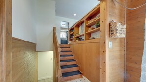Un escalier en bois, avec des marches décorées, mène à une pièce où se trouvent des étagères et des paniers.
