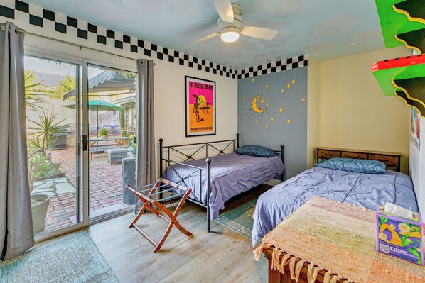 A bedroom with a bed, a ceiling fan, a poster, and a view of the outside.