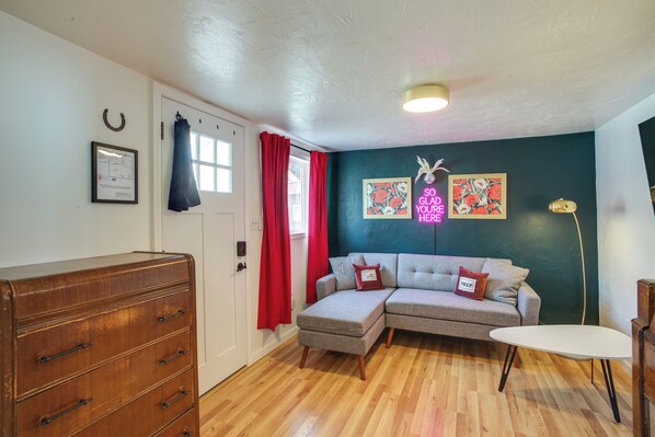 A room with a wooden dresser, a grey sectional sofa, a small white table, and a neon sign on the wall. - Unit 4: Central 1-br, New Bath, 3 Mi to Dtwn (Spokane)