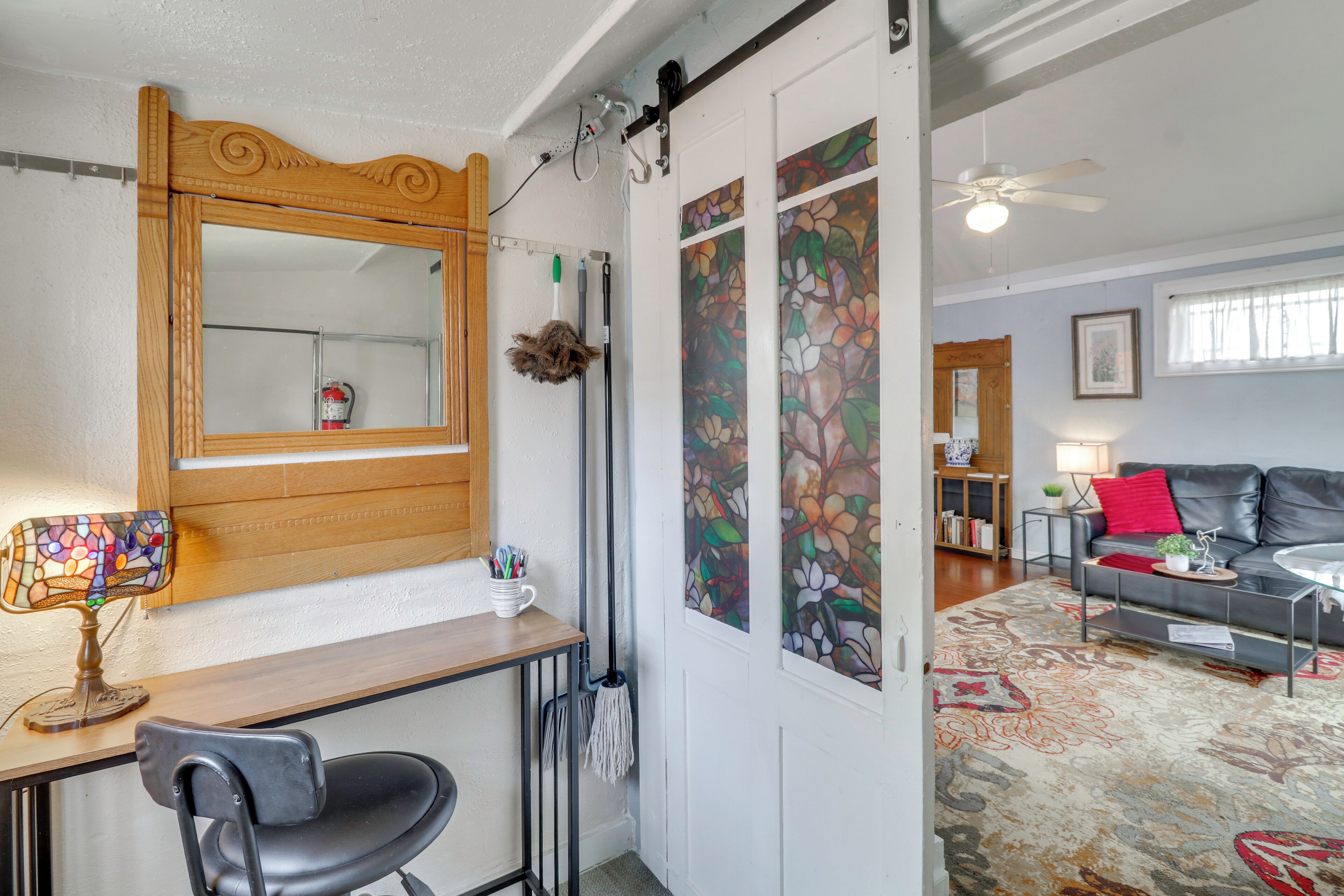 A room with a wooden desk, chair, mirror, and a large window with floral artwork.