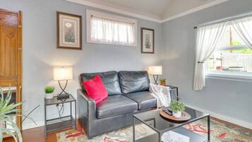 A living room with a black leather sofa, two side tables with lamps, a glass coffee table, and a patterned rug.