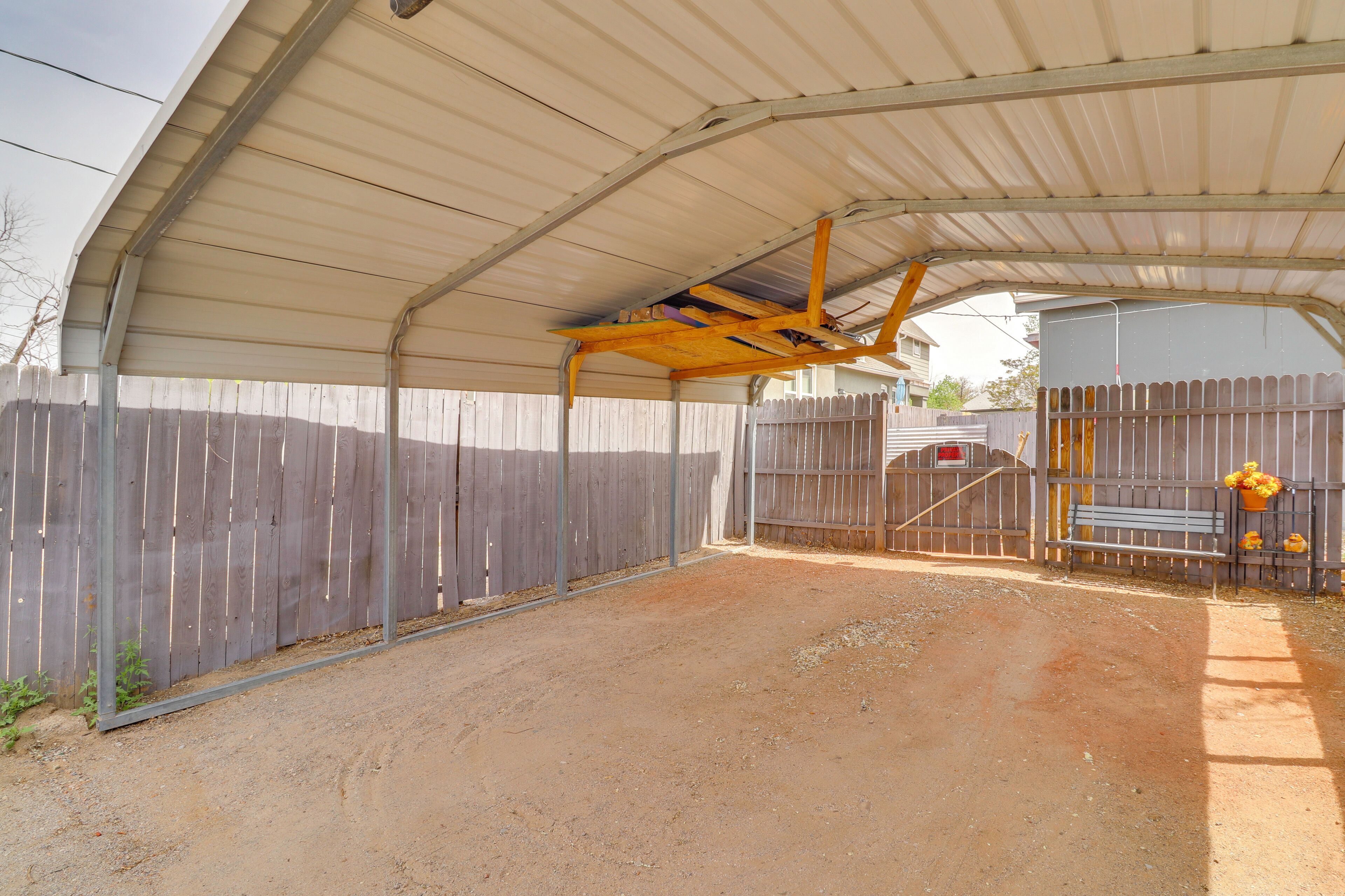 A covered outdoor area with a dirt ground, metal roof, and wooden fence.