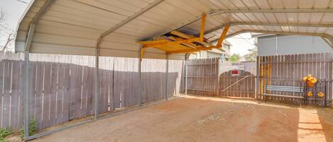 A covered outdoor area with a dirt ground, metal roof, and wooden fence.