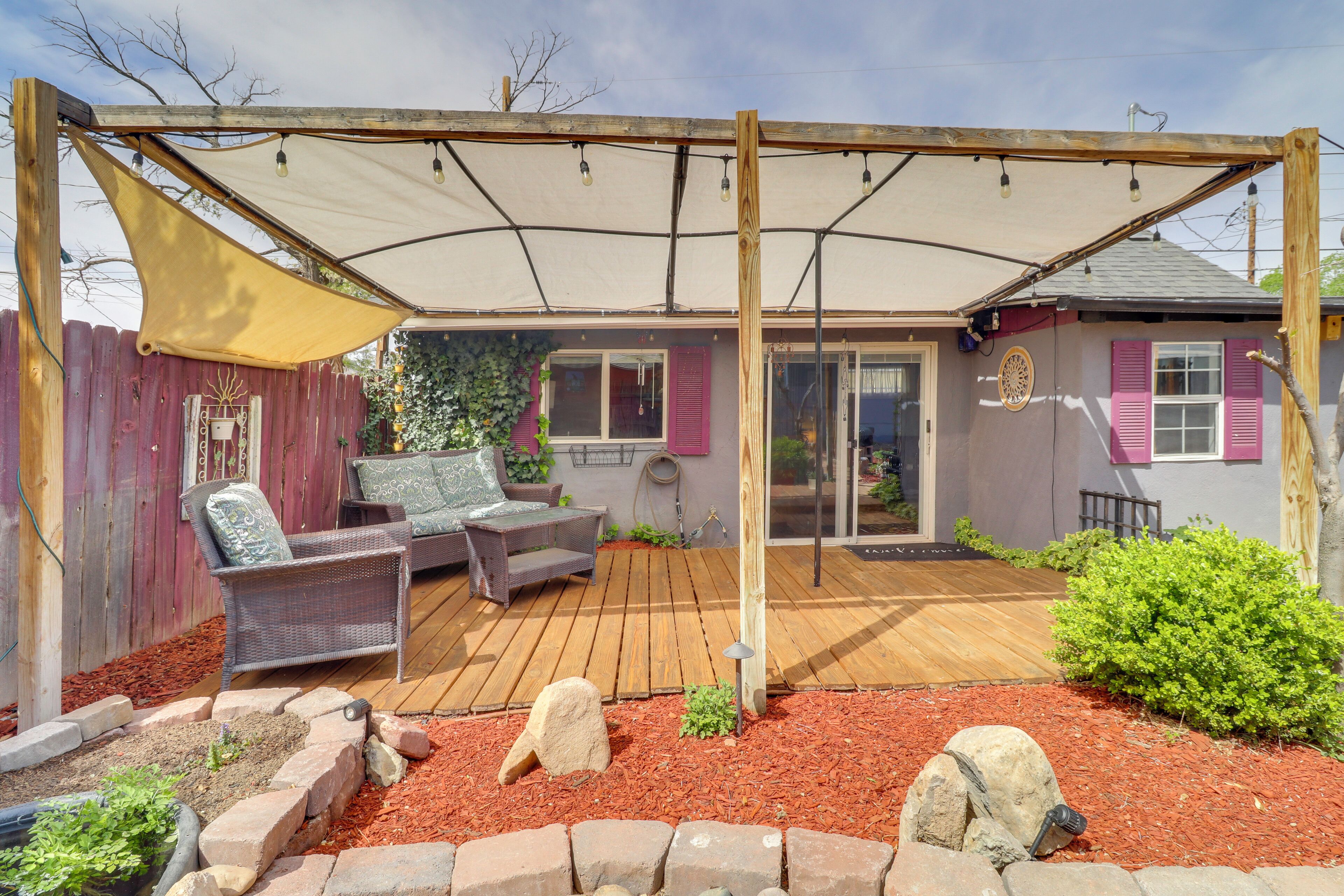 A covered patio with outdoor furniture, a wooden deck, and a garden area with mulch and rocks.