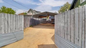 A fenced backyard with a corrugated metal wall, a covered area, and a house in the background.