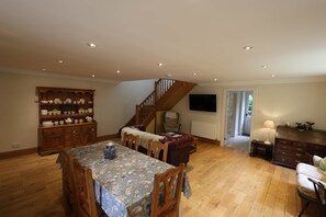 Ein geräumiger Wohnbereich mit Esstisch, Holzkästen, einer Couch, einer Treppe und einem an der Wand befestigten Fernseher.