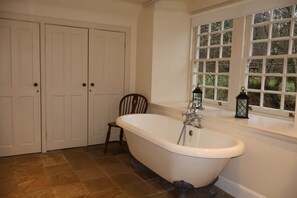 A bathroom with a freestanding bathtub, a window with a view of trees, and a wooden chair. - Forget Me Not - Craigengillan Estate (Dalmellington)