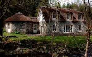 A stone house with a thatched roof, a stone porch, and a grassy yard. - Forget Me Not - Craigengillan Estate (Dalmellington)