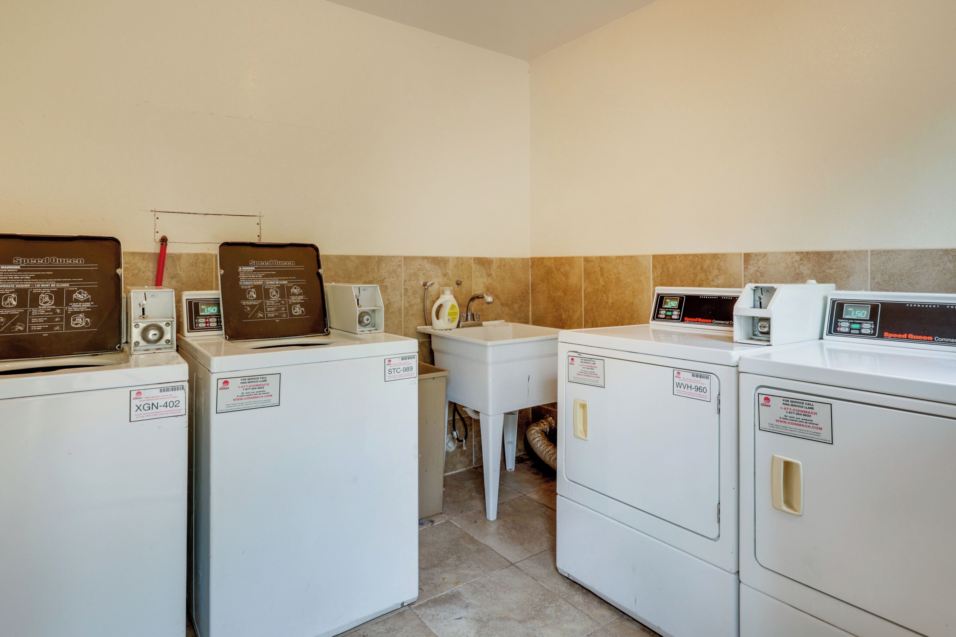 A laundry area with four washing machines, a white sink, and a towel rack.