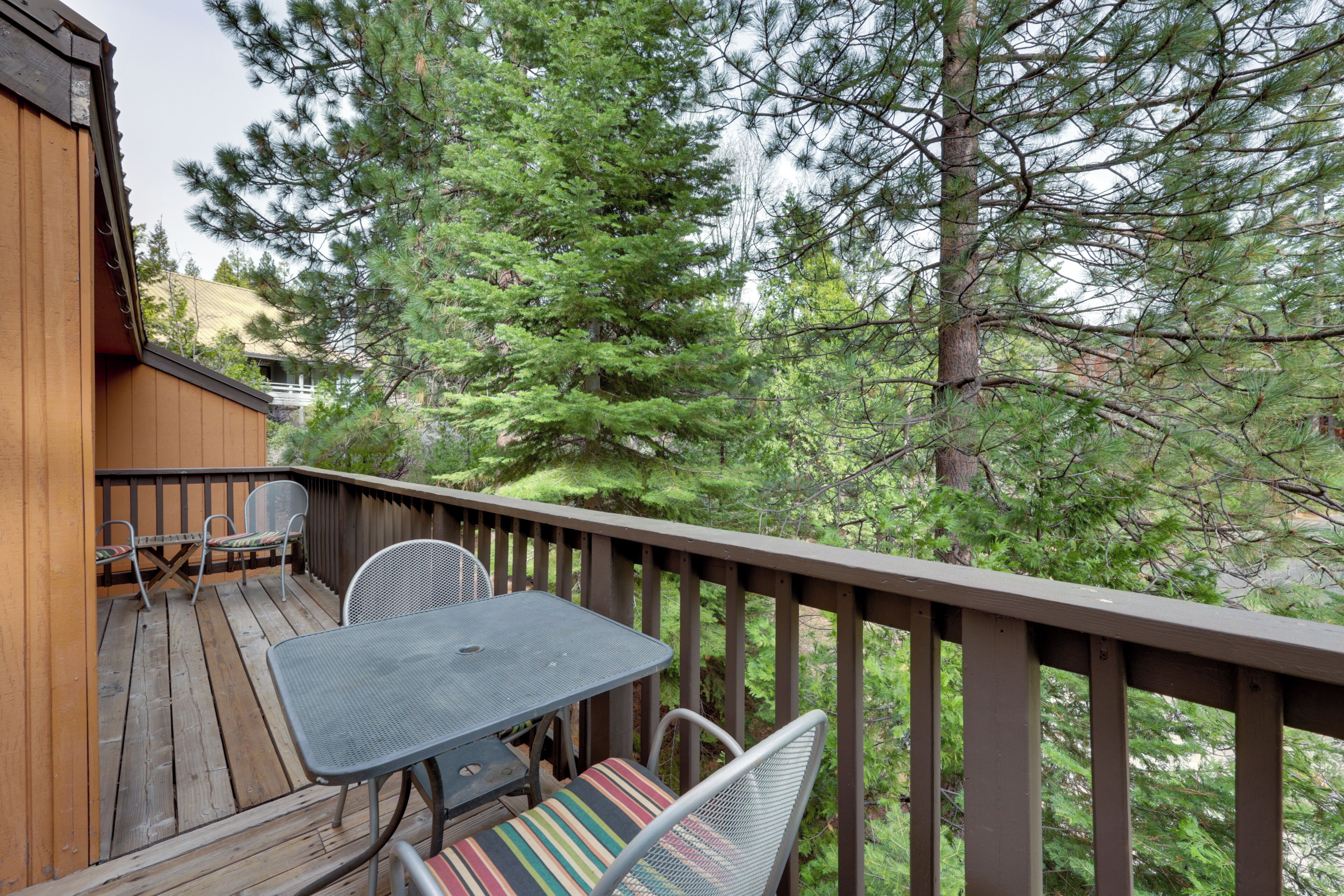 A wooden deck with a table and chairs, surrounded by tall trees.