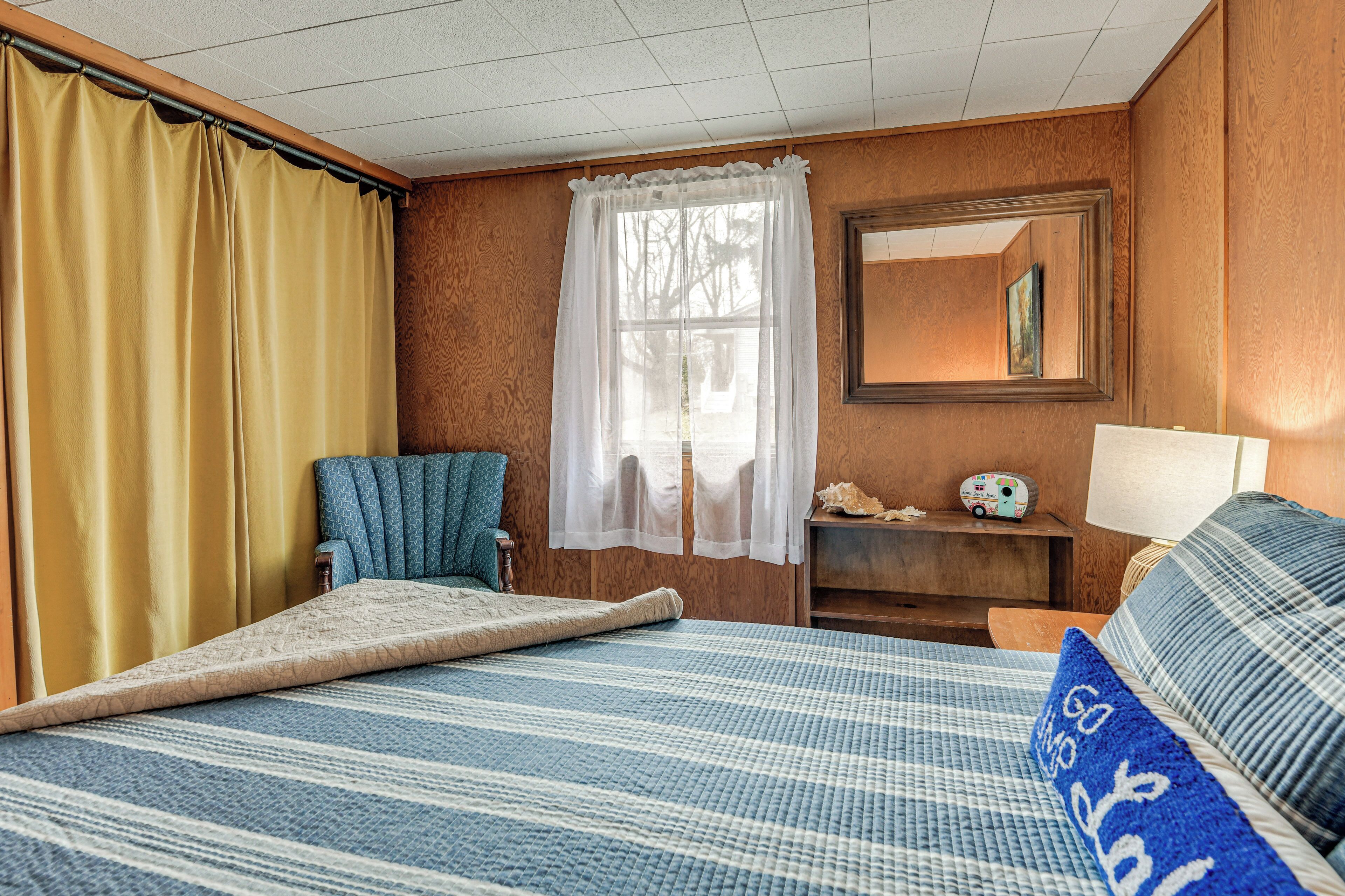 Een kamer met een bed, een stoel, een raam met gordijnen, een spiegel en een lamp.