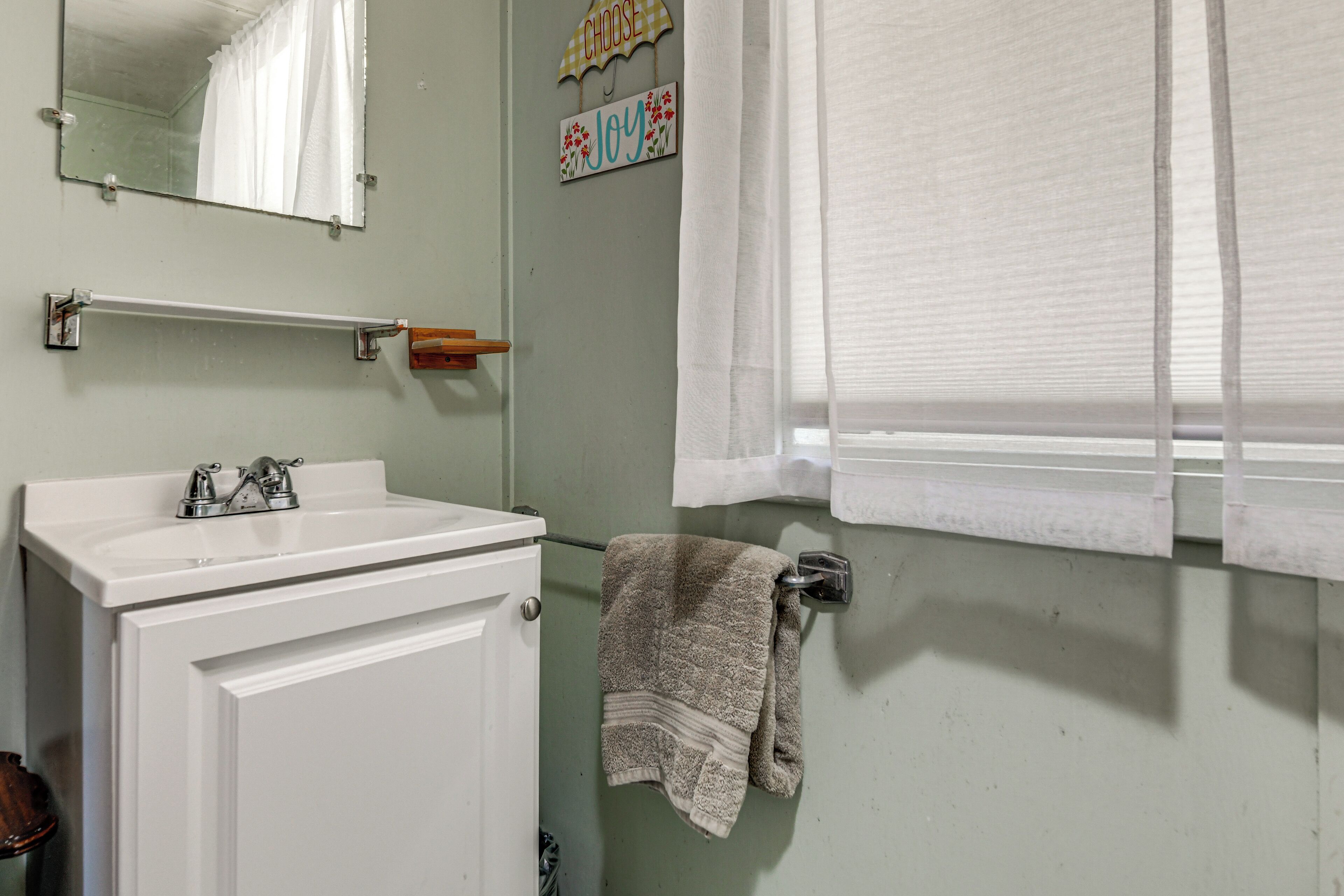 A bathroom with a white sink, mirror, towel rack, and a window with blinds.