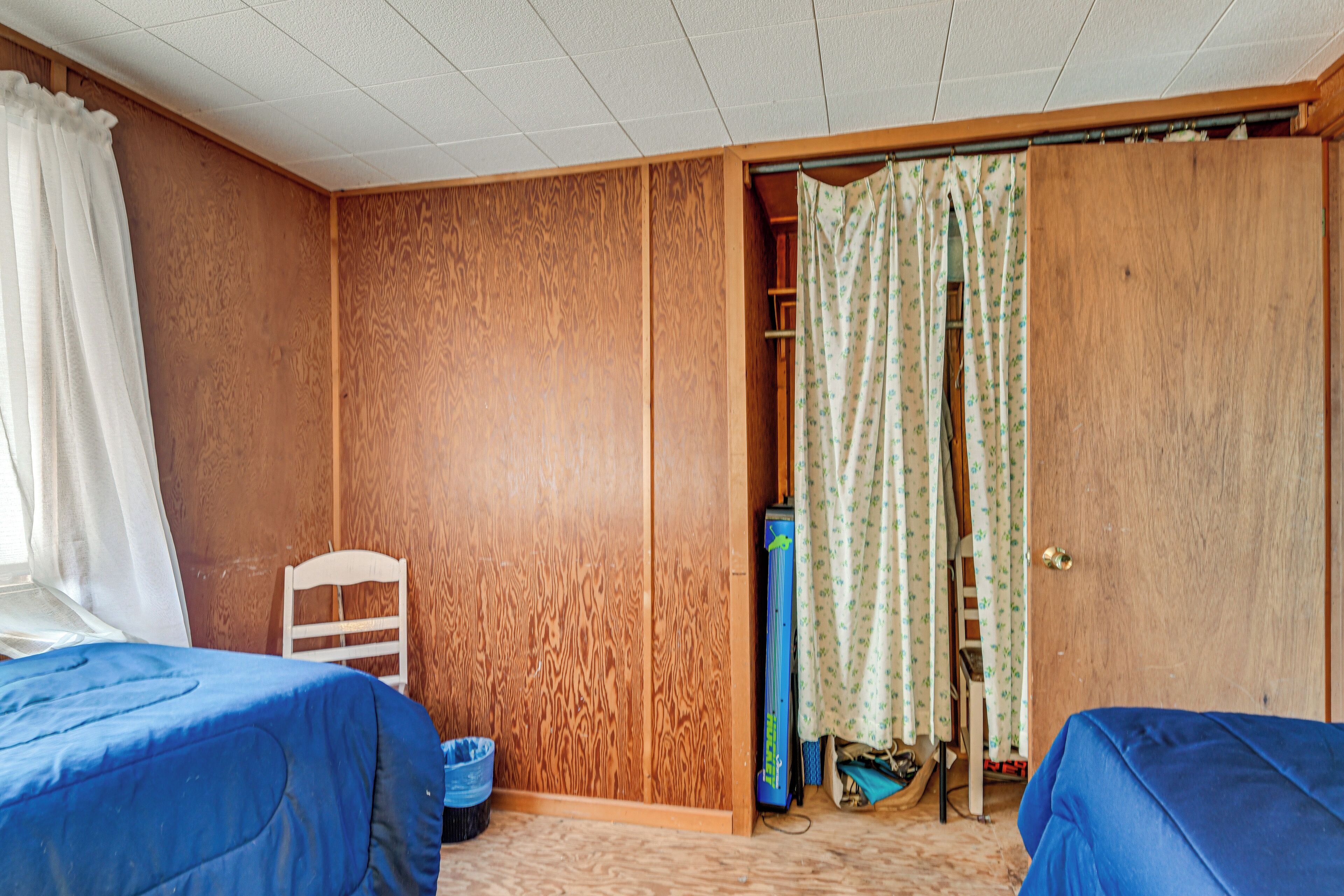 A room with two beds, a wooden wardrobe, a chair, and a window with curtains.