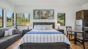 Een slaapkamer met een groot bed, een sofa, een eettafel en een keukenhoek. Er hangen drie ingelijste foto’s aan de muur.