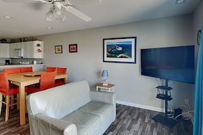 A living room with a sofa, dining table with chairs, a TV, and a ceiling fan. - Lazy Daze | Intercoastal Views + Pool Access (Surf City)