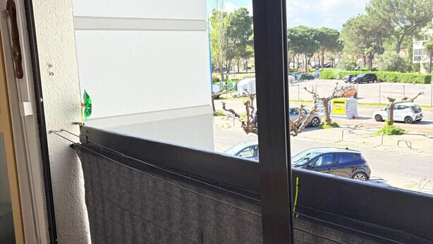 Une chambre d’hôtel avec une grande fenêtre, donnant sur un parking, et un sol recouvert de carreaux rouges.