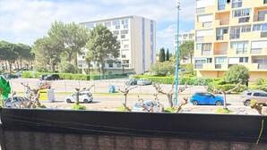 Vue depuis l’intérieur d’un bâtiment, donnant sur un parking avec des voitures et des immeubles en arrière-plan.