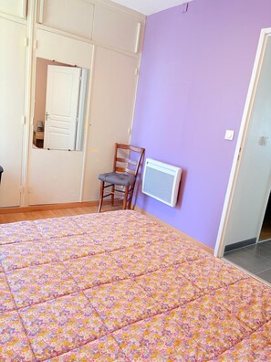 Een slaapkamer met een bed, een stoel, een radiator en een deur.