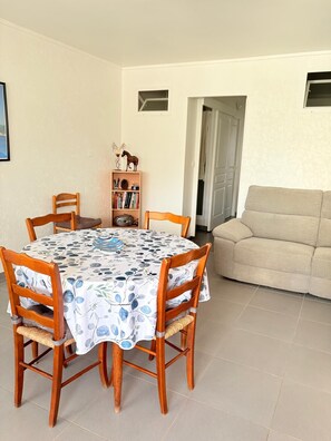 Een eethoek met een ronde tafel, houten stoelen, een boekenkast en een beige bank.