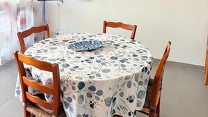 Un coin repas avec une table ronde, quatre chaises en bois, un téléviseur à écran plat fixé au mur et un tableau représentant un paysage côtier.