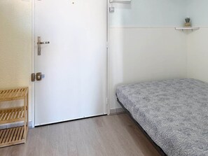 Une pièce avec un lit, un banc en bois, une porte blanche et une étagère sur laquelle se trouve une plante.