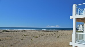 Vista de una playa con una estructura blanca, posiblemente una torre de salvavidas, y una casa al fondo.