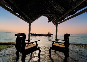 A stone-paved area with two wooden chairs facing a calm body of water.