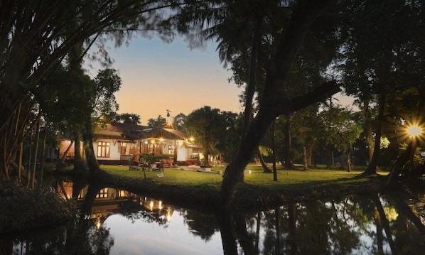 Un bâtiment avec un bassin aux reflets changeants, entouré d’arbres et illuminé par le coucher de soleil.