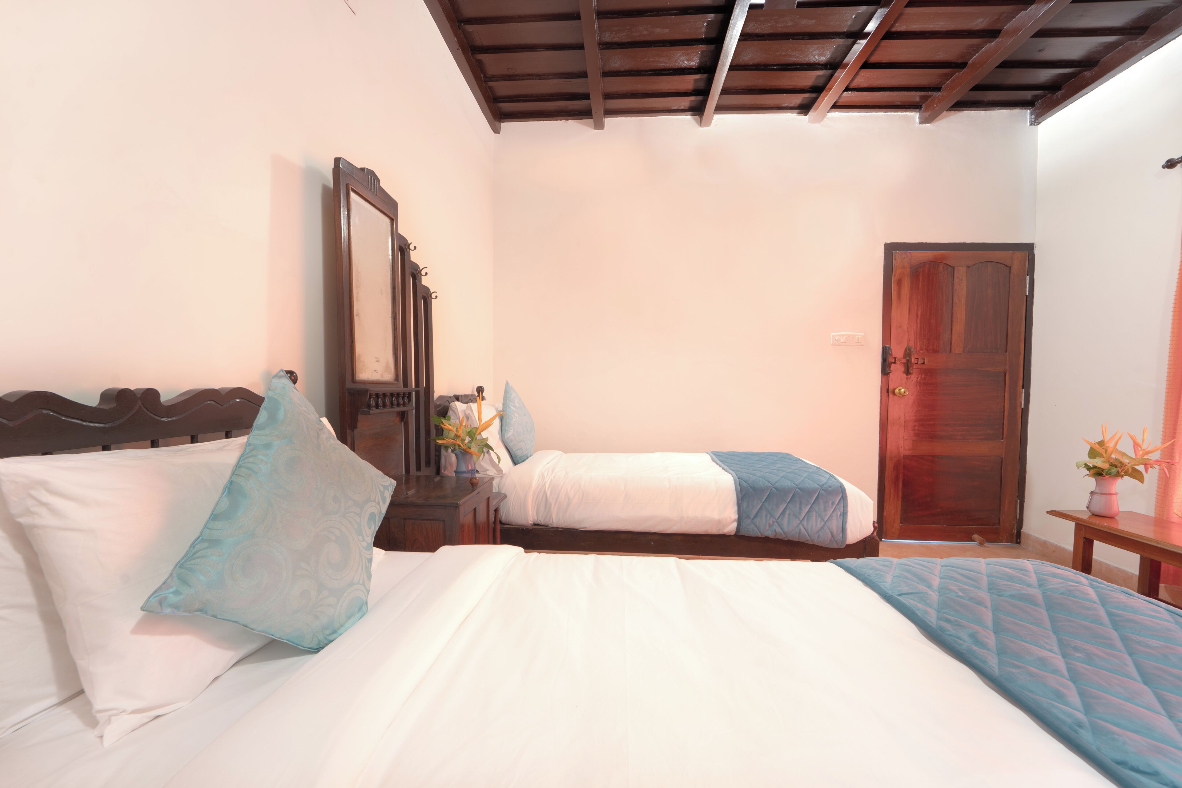 A bedroom with two beds, a wooden headboard, a bedside table with a mirror, and a door.