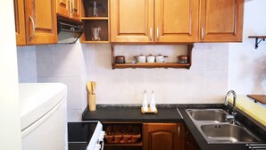 Eine Küche mit Holzausstattung, einer schwarzen Arbeitsplatte, einem Edelstahl-Spülbecken und einem eingebauten Backofen.
