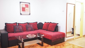 Ein Wohnzimmer mit einer schwarzen Couch, roten Kissen, einem Glastisch und einem gerahmten Bild an der Wand.