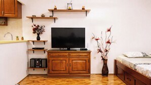 Ein kompakter Wohnraum mit Fernseher, Holzschrank und einem Bett.