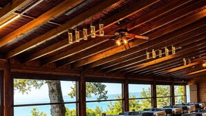 Ein Restaurant mit Holzbalkendecke, Tischen mit weißen Tischdecken und Blick aufs Meer.