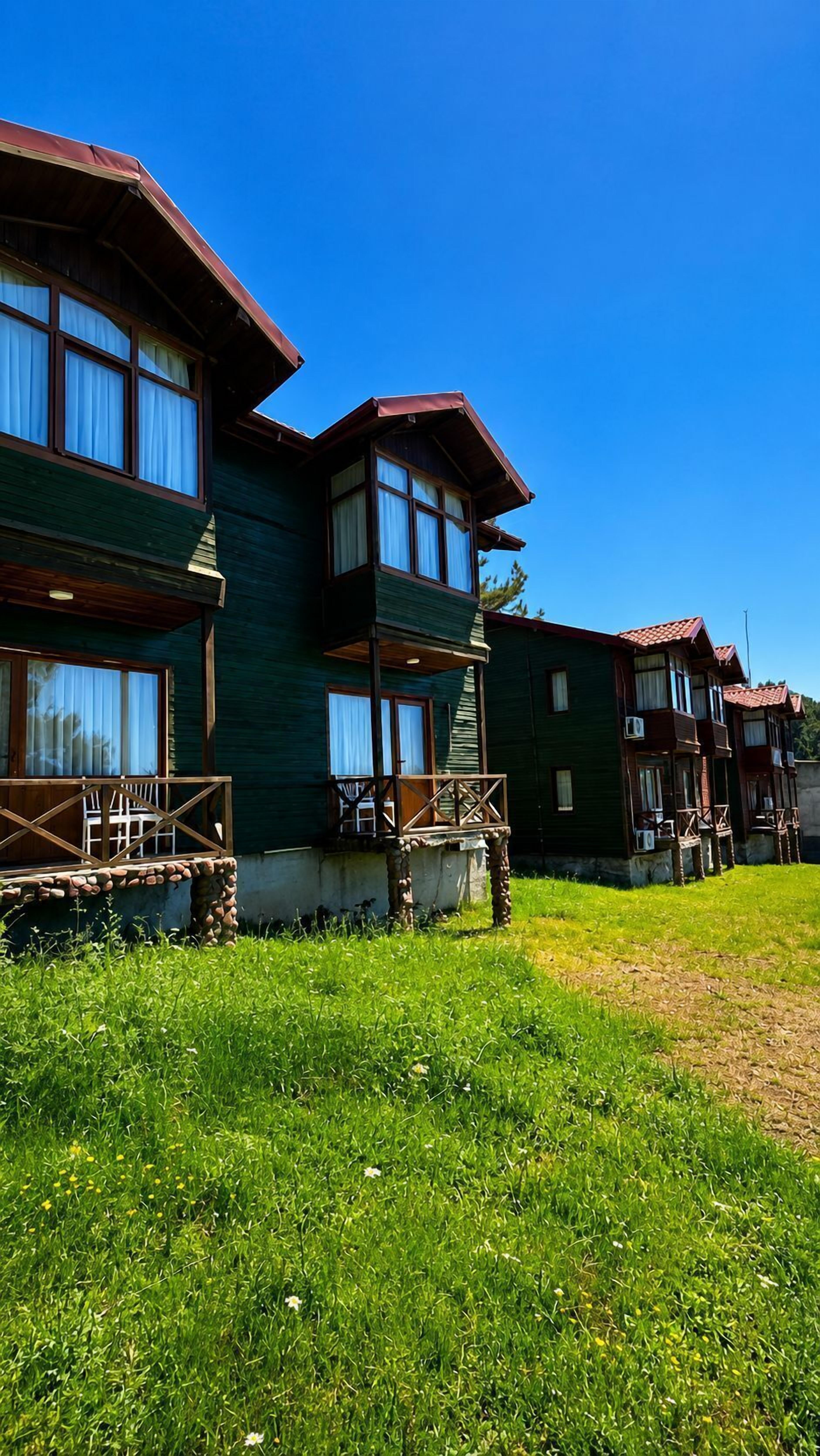 A row of wooden buildings with balconies, a grassy lawn, and a clear blue sky.