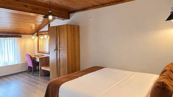 Habitación de hotel con techo de madera, cama con edredón blanco, escritorio con silla y ventana con cortinas.