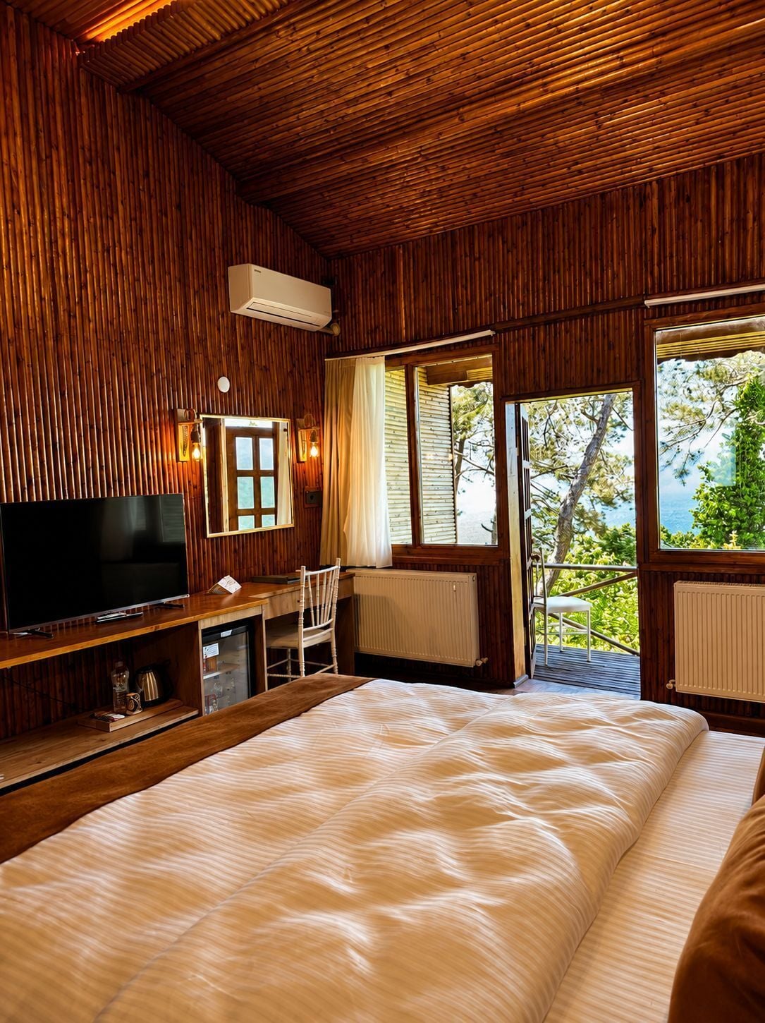 Una habitación de madera con una cama, un televisor, un escritorio y una ventana con vistas.