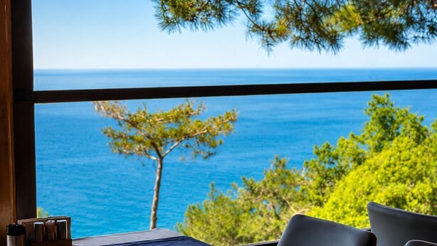 Ein Zimmer mit großem Fenster und Meerblick, ein Bett sowie ein Tisch mit Stühlen.