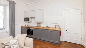 A compact kitchen with grey cabinets, a wooden countertop, a built-in microwave, and a sink. - Stylish West End 1-Bed | Prime Location (Edinburgh)
