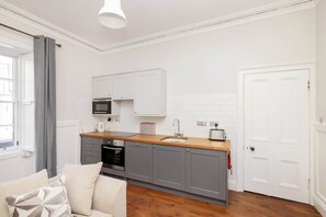 A compact kitchen with grey cabinets, a wooden countertop, a built-in microwave, and a sink. - Stylish West End 1-Bed | Prime Location (Edinburgh)
