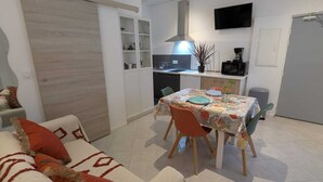 Ett kompakt bostadsutrymme med en matplats, ett litet kök och en soffa med kuddar.