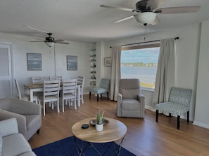 A living room with a dining area, two ceiling fans, a large window with a view of the water, and a blue rug. - 3 bedroom 2 bath lagoon front condominium Gulf Shores (Gulf Shores)